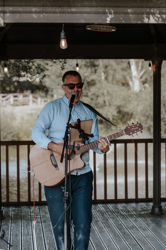 Matthew singing and playing acoustic guitar beneath a covered outdoor terrace