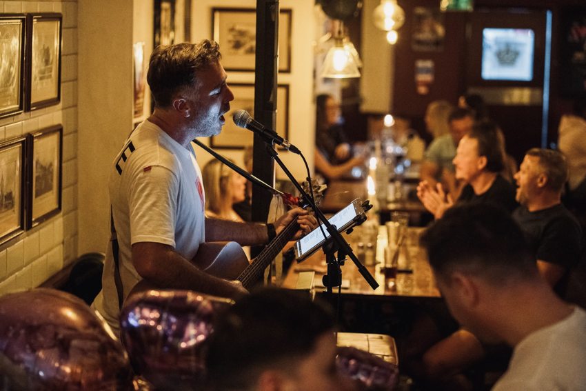 Side view of Matthew singing and playing guitar with guests joining in