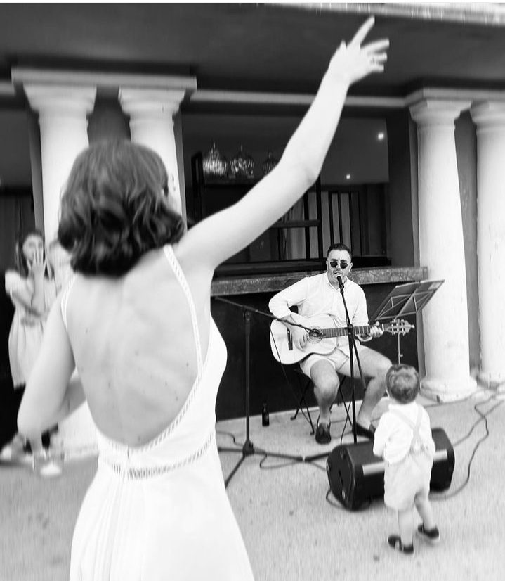 A bride with her arm raised while Matthew performs acoustic guitar nearby
