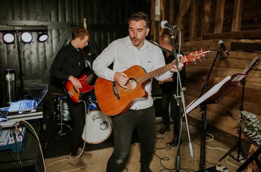 Matthew performing guitar with a bass guitarist and drummer in a timber-lined venue
