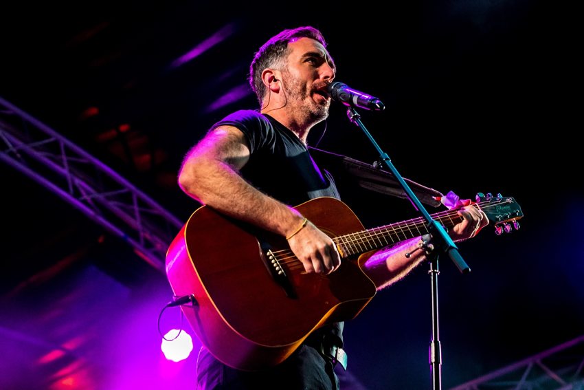 Matthew singing and playing guitar on stage under purple concert lighting