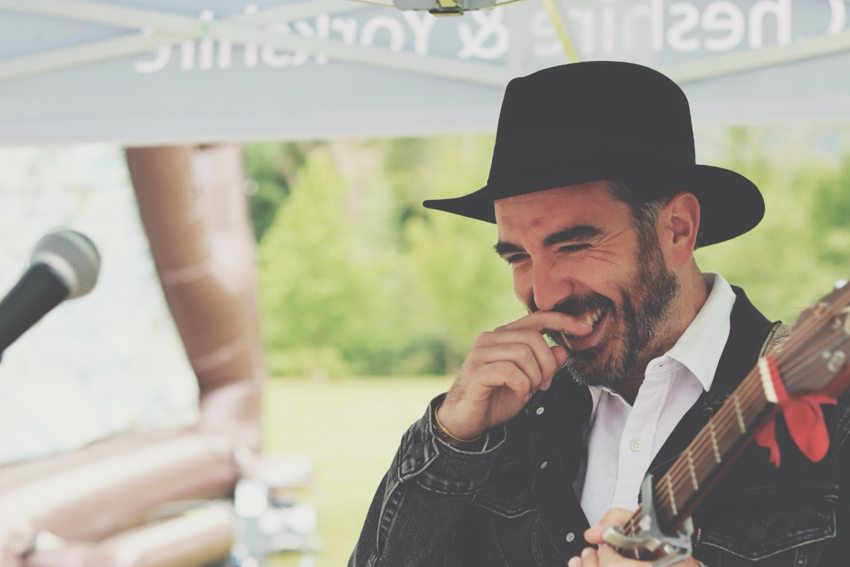 Matthew smiling with his guitar beside a microphone during an outdoor performance