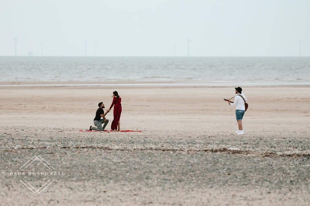 Matthew playing acoustic guitar on the beach as a couple get engaged