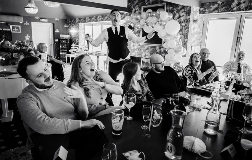Black-and-white photograph of Matthew as a singing waiter with guests singing at their tables